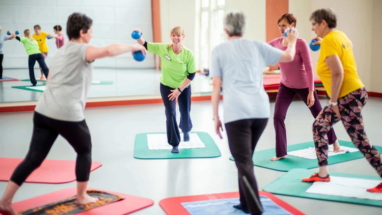 Therapeutin trainiert mit Pateintengruppe in der Bewegungstherapie