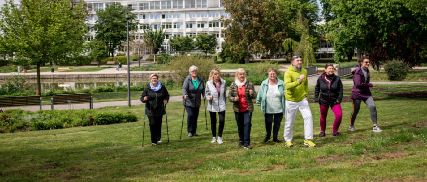 Patientengruppe und Therapeut beim Nordic Walking in der Nähe der Klinik